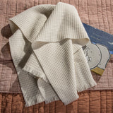 Folded beige 100% merino wool baby blanket on a textured surface with a children's book underneath