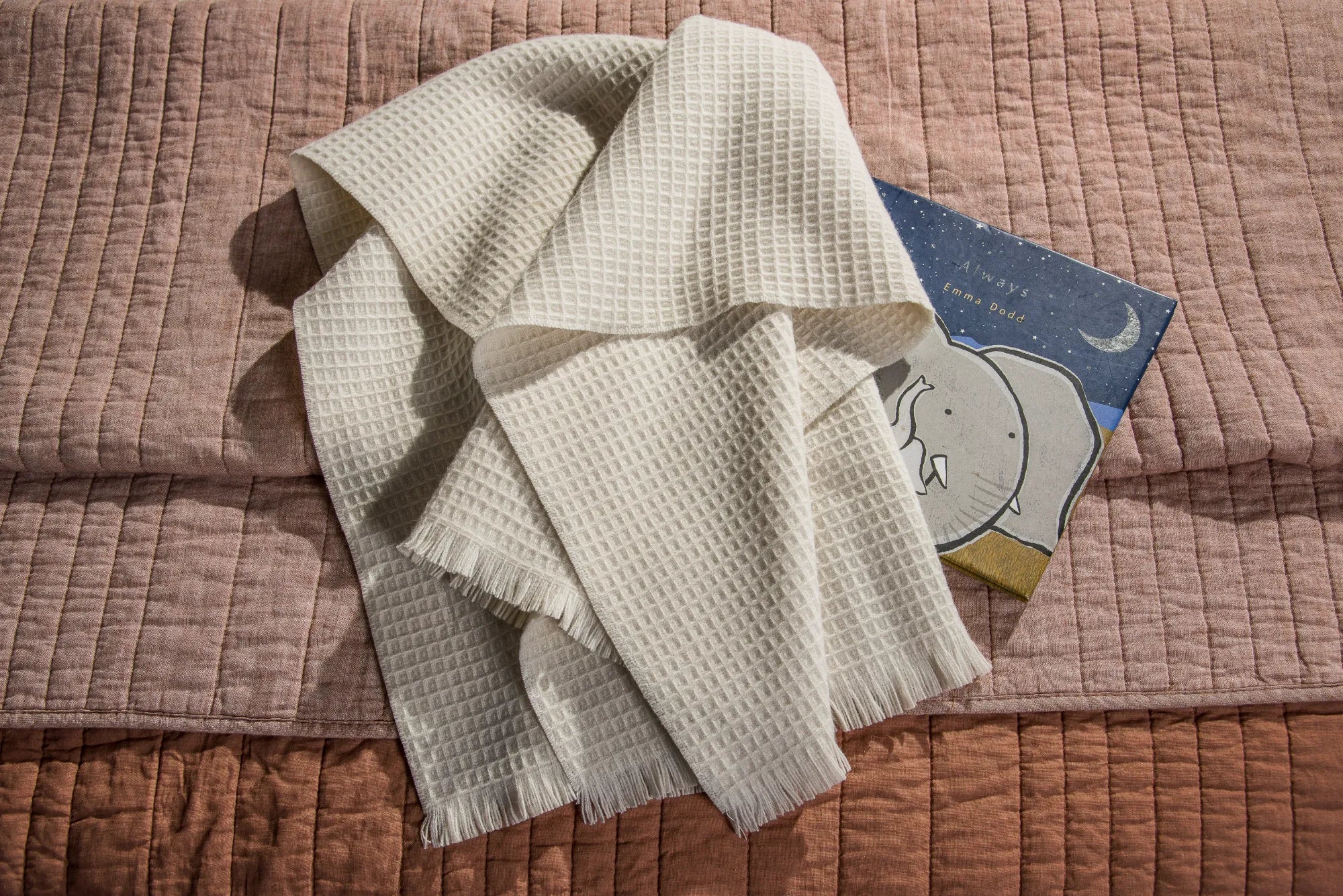 Folded beige 100% merino wool baby blanket on a textured surface with a children's book underneath