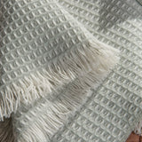 Textured 100% merino wool baby blanket with fringes on a brown sofa.
