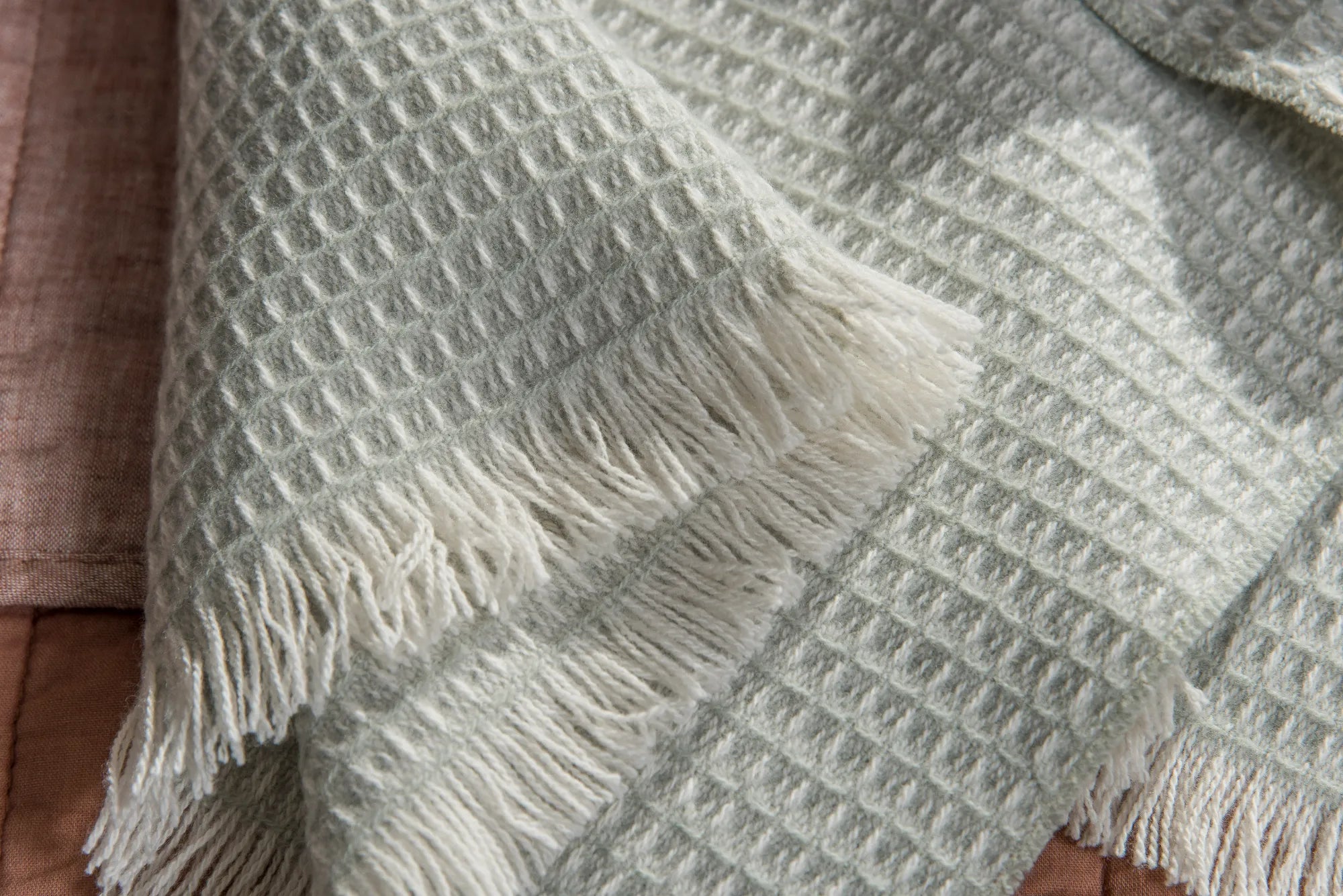 Textured 100% merino wool baby blanket with fringes on a brown sofa.