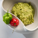 Guacamole in a ceramic Cuenko bowl with green and red peppers on a white tabletop