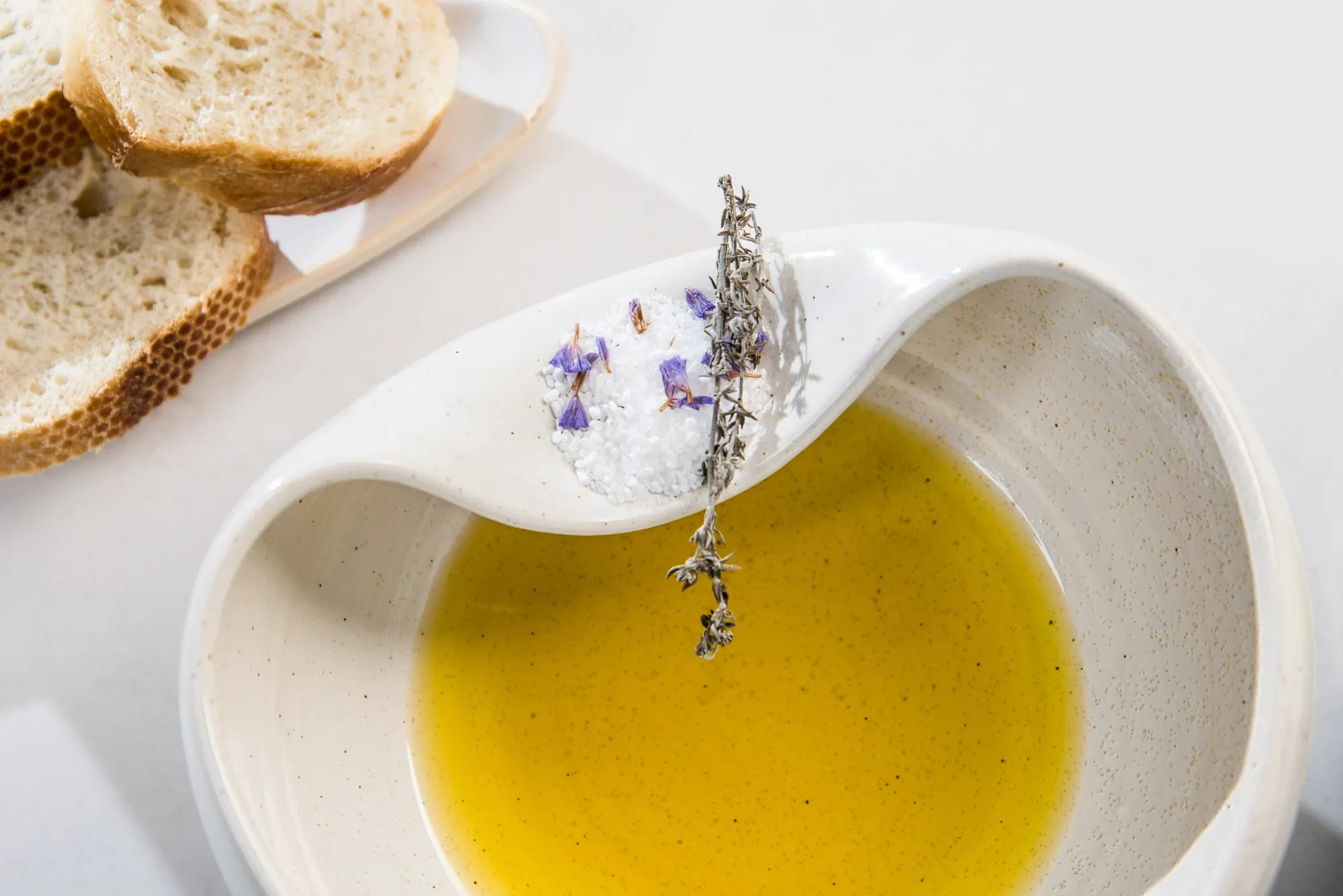 Ceramic Cuenko bowl of olive oil with a lavender sprig, bread slices on a white plate.