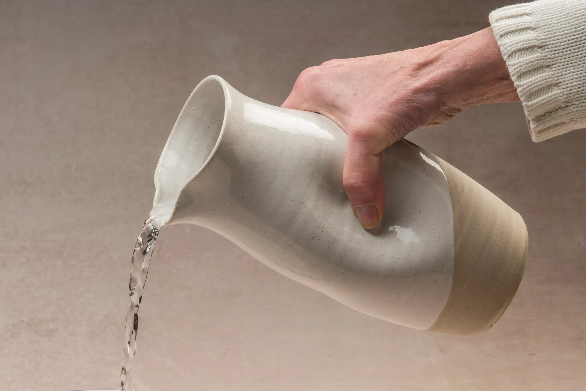 Hand pouring water from a ceramic Jarra pitcher on a neutral background