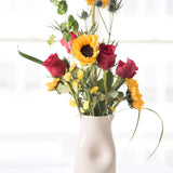 Floral arrangement with sunflowers and red roses in a Jarra pitcher vase on a light background
