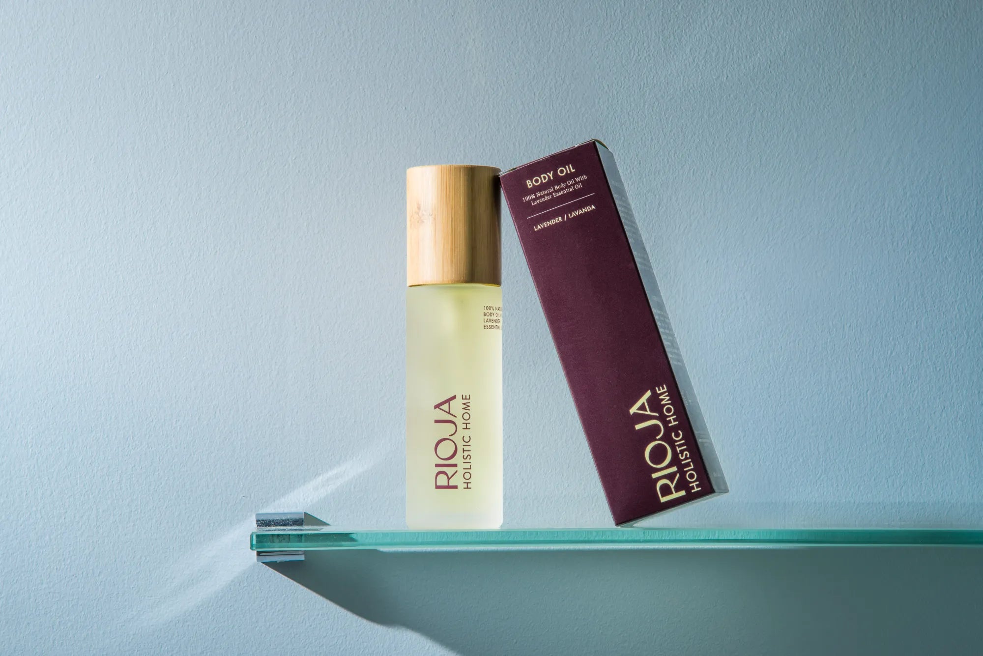 Rioja body oil bottle and box on a glass shelf against a light blue background