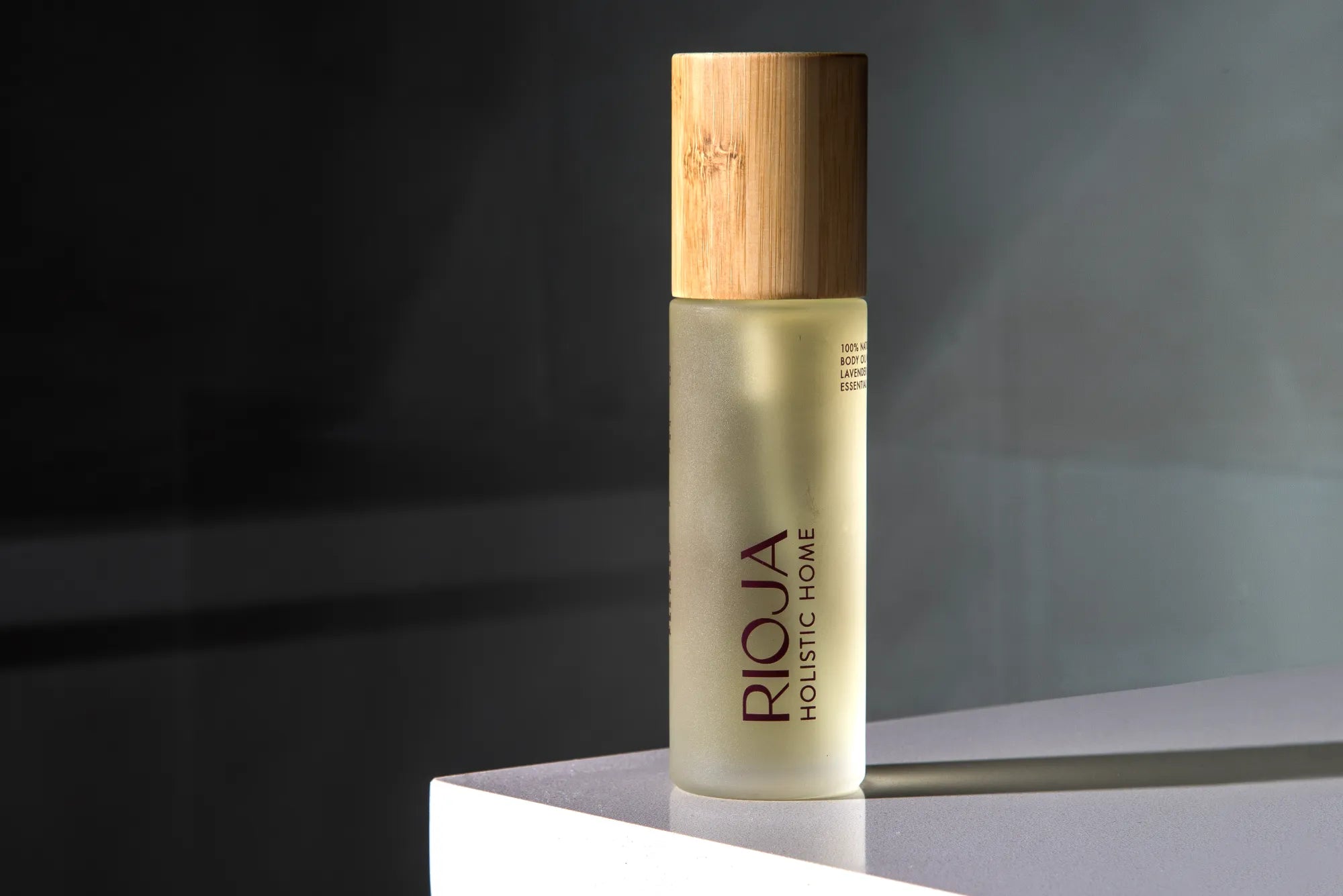 Body oil bottle with wooden cap on a dark background by Rioja Holistic Home