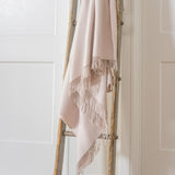 Beige 100% merino wool blanket draped over a wooden ladder against a white wall.
