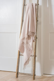 Beige 100% merino wool blanket draped over a wooden ladder against a white wall.