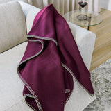 Plum 100% merino wool blanket draped over a white sofa with a glass table and wine glass in the background.