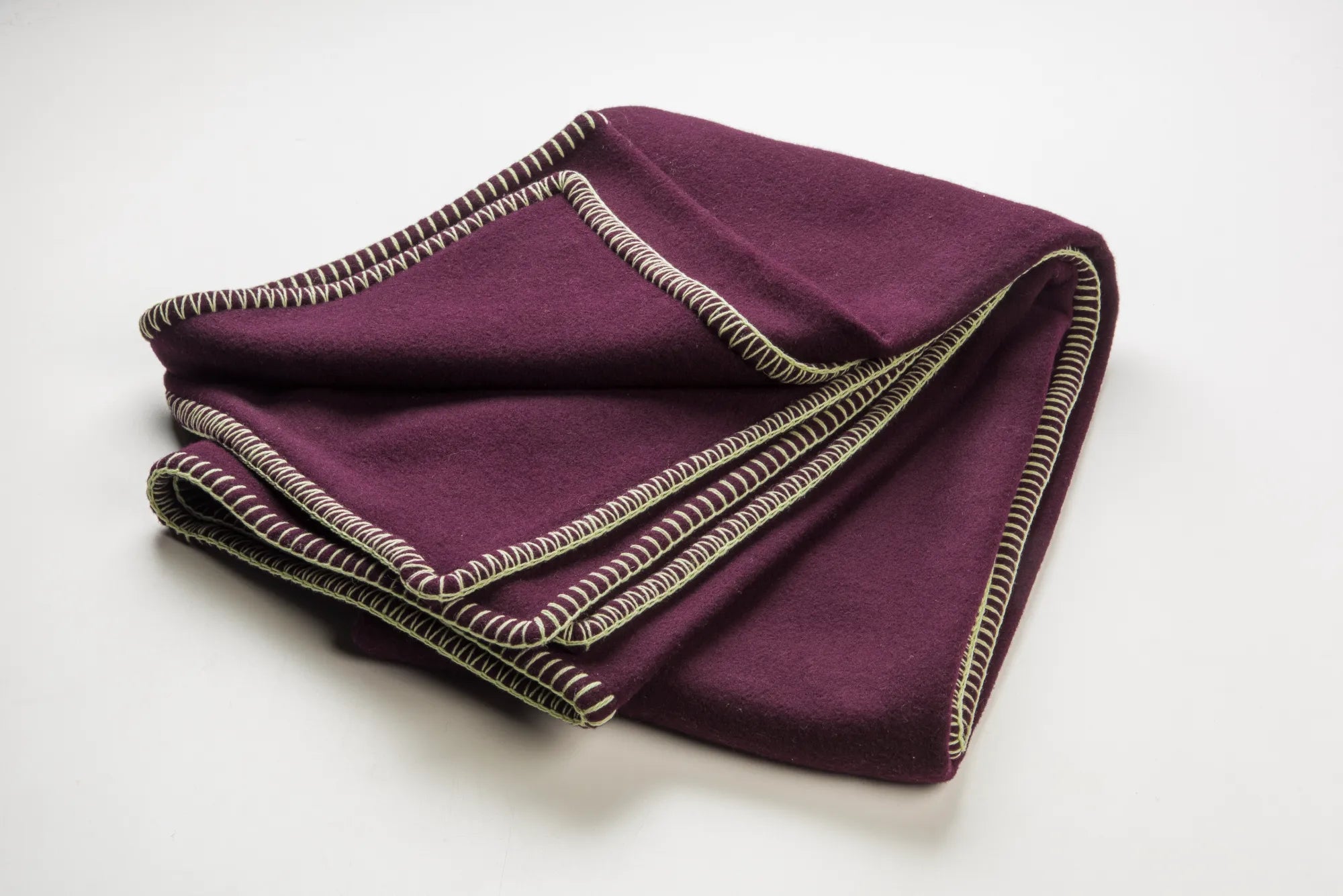 Folded plum 100% merino wool blanket with green and beige trim on a white background