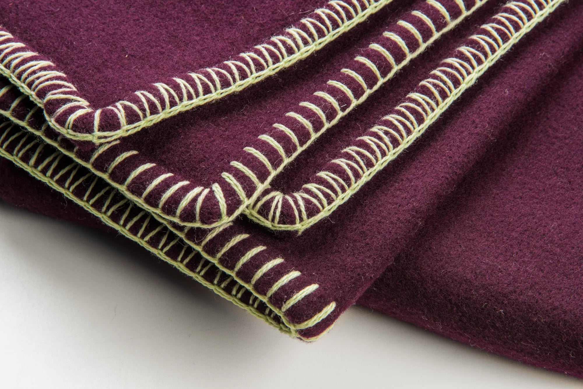 Close-up of a plum 100% merino wool blanket fabric with green embroidery on a white background