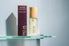 Riqa Holistic Home body oil bottle and packaging on a glass shelf with a gray background