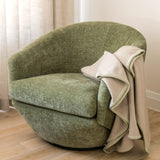 Green armchair with a beige 100% merino wool blanket in a room with a wooden side table and wine glass.