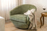 Green armchair with a beige 100% merino wool blanket in a room with a wooden side table and wine glass.