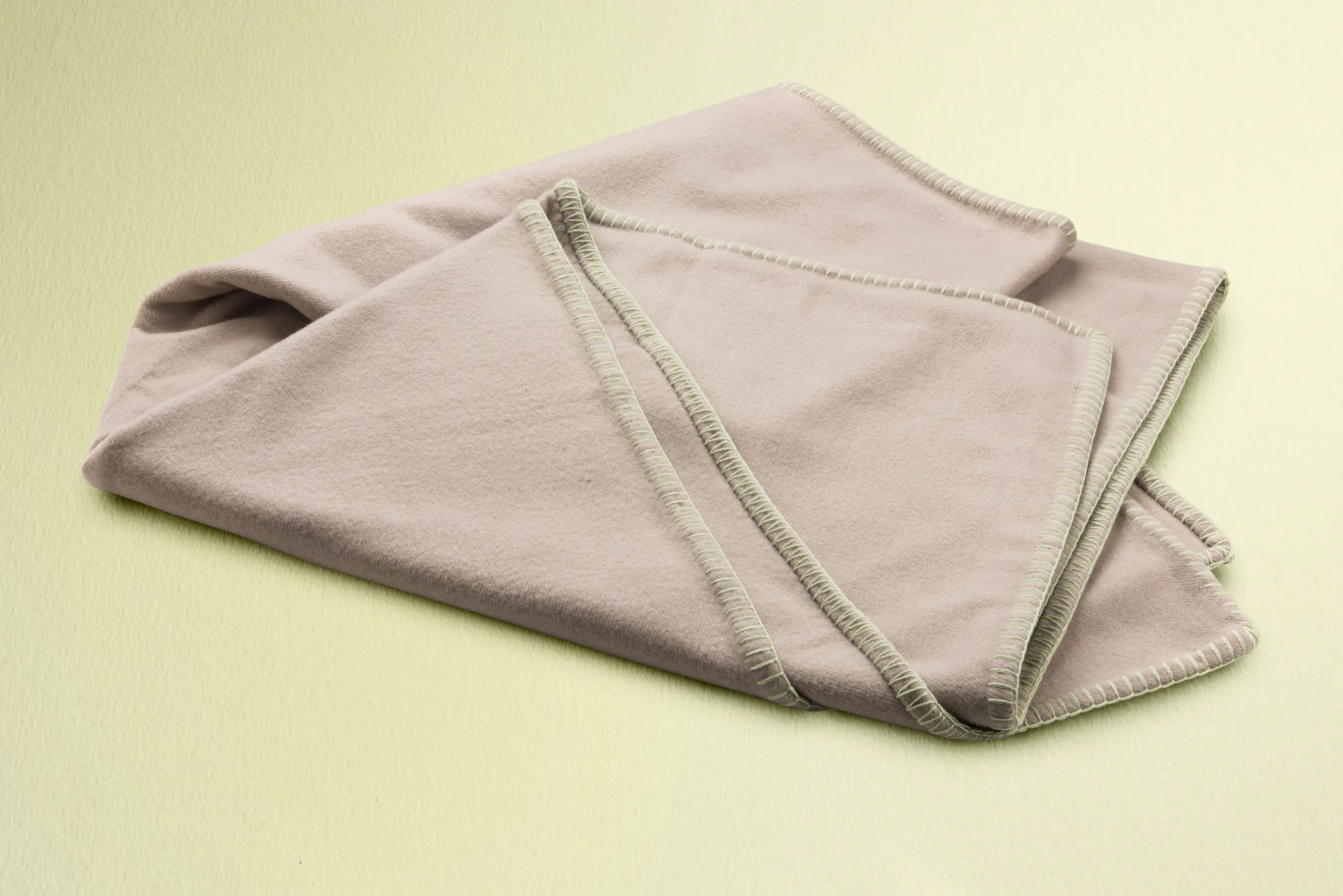 Folded beige 100% merino wool blanket on a light green background