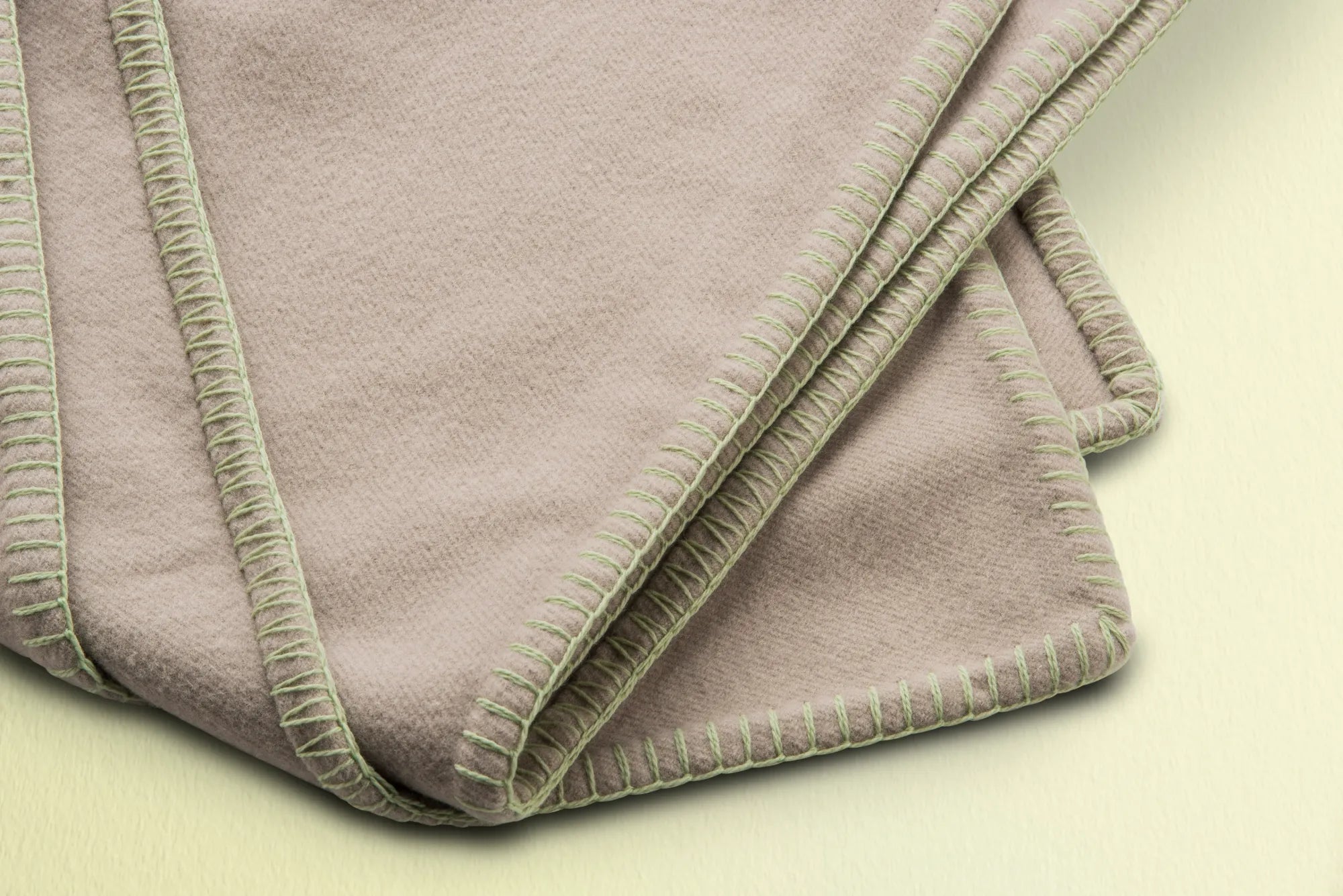Folded beige 100% merino wool blanket on a light green background
