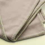 Folded beige 100% merino wool blanket on a light green background