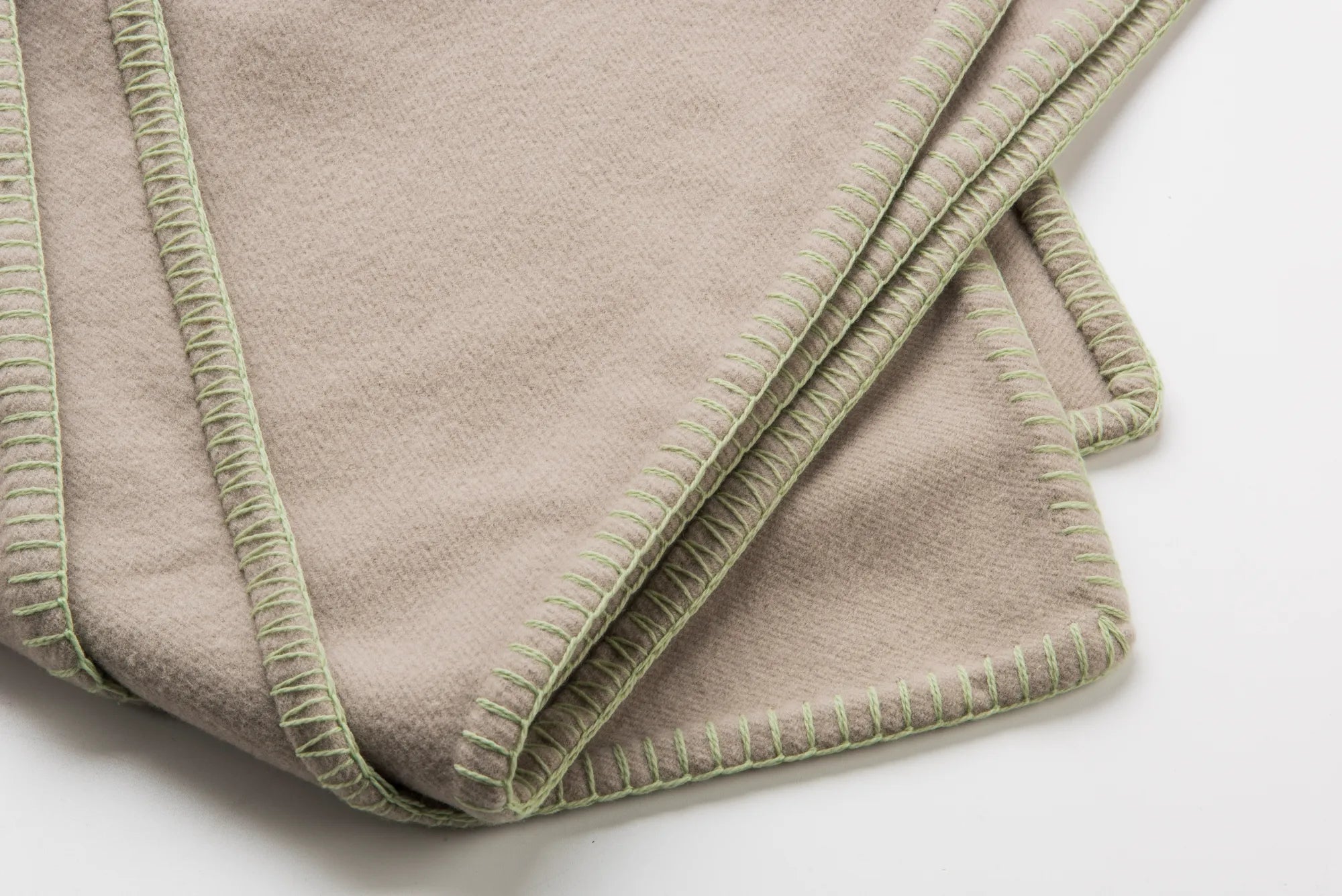 Folded beige 100% merino wool blanket with green trim on a white background